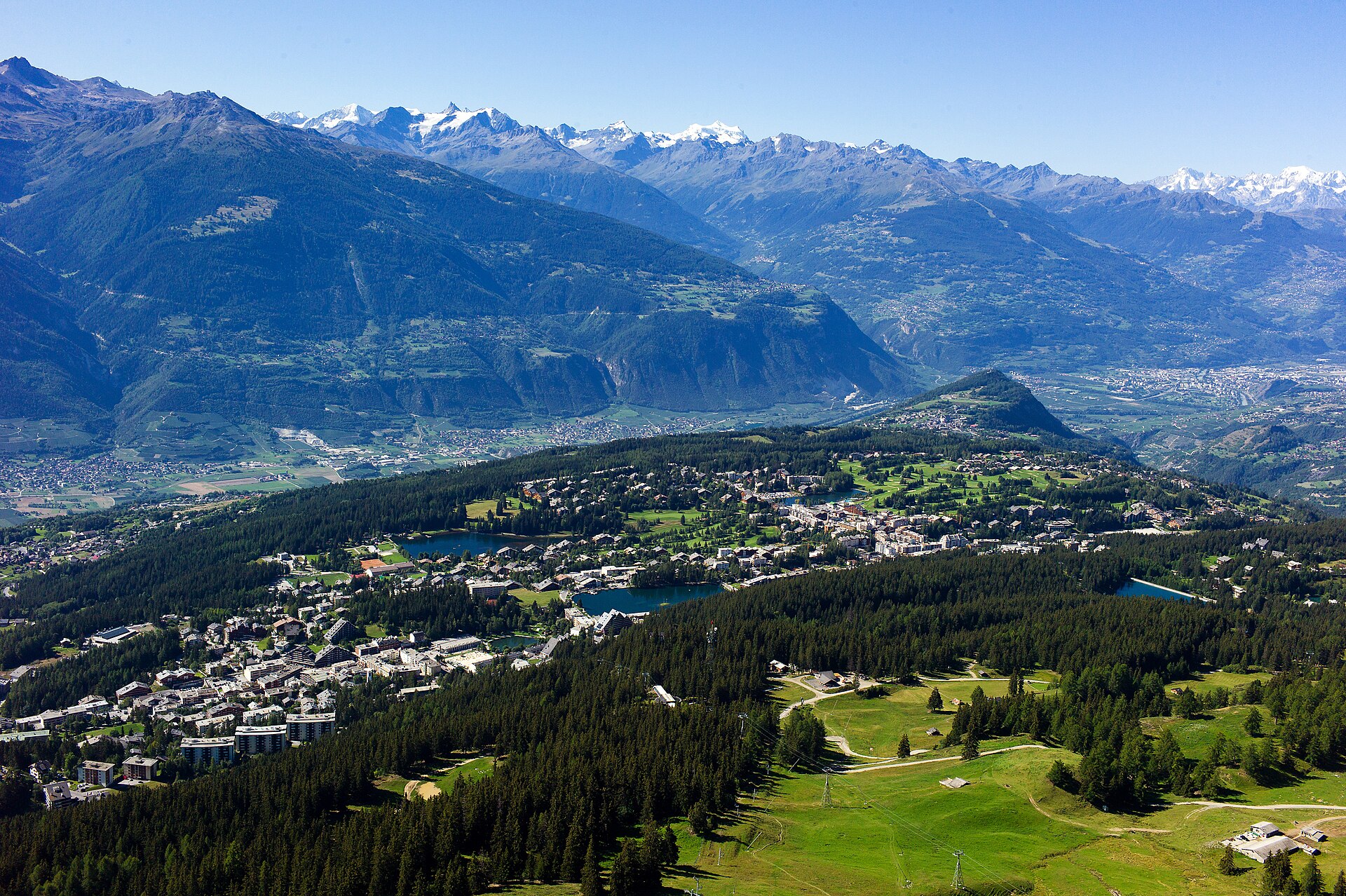 Vue aérienne estivale du plateau de Crans-Montana, ses lacs et la chaîne des Alpes valaisannes